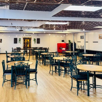 Large room with tables and chairs arranged for events or meetings, with a red sofa and decorative elements on the walls.